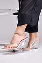 scarpin-anabela-feminina-vinil-prata-storm Detalhe dos pés com Scarpin Anabela Feminina Vinil Prata - Storm, calça preta fluida e tornozeleiras douradas, apoiado em cadeira metálica cromada