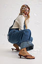 gummy-tamanco-feminino-transparente-salto-baixo-marrom Tamanco Feminino Flip Flop Gummy marrom em PVC translúcido, modelo agachada usando macacão jeans, vista lateral completa