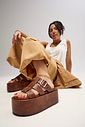 bangkok-tamanco-feminino-camel Modelo sentada no chão, com regata branca e calça bege e tamanco camelfashionista