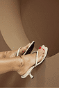 hanna-tamanco-feminino-off-white Tamanco Feminino Couro Dedo Salto Hanna off white nos pés, foto de detalhe lateral mostrando o salto fino curvado, tiras e bico irregular