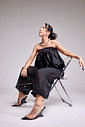 tamanco-feminino-tiras-de-vinil-preto-miranda Modelo sentada em cadeira acrílica, look total black tomara que caia, calçando o Tamanco Feminino Tiras de Vinil Preto - Miranda, corpo inteiro