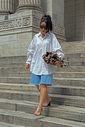 tamanco-feminino-tiras-de-vinil-marrom-miranda Modelo em look de rua descendo escadaria com camisa branca oversized e short jeans azul, usando o Tamanco Feminino Tiras de Vinil Marrom - Miranda.