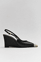 Slingback Feminino Naomi Preto Lateral Slingback feminino Naomi preto em vista lateral, com salto anabela de aproximadamente 9 cm, bico fino com ponteira metálica dourada e tira traseira com fivela ajustável.