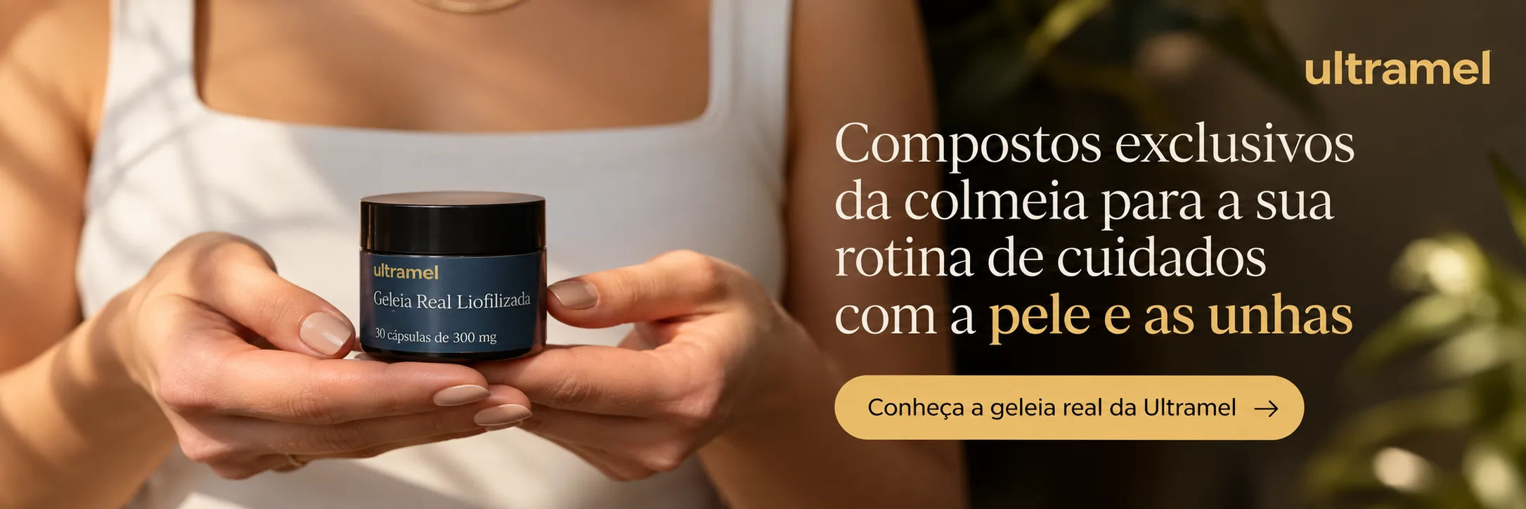 Uma pessoa de camiseta regata branca segura com as duas mãos um pote preto com rótulo azul-marinho que traz a marca "ultramel", o texto "Geleia Real Liofilizada" e "30 cápsulas de 300 mg". Ao lado, o texto em destaque diz "Compostos exclusivos da colmeia para a sua rotina de cuidados com a pele e as unhas" e o botão "Conheça a geleia real da Ultramel →".