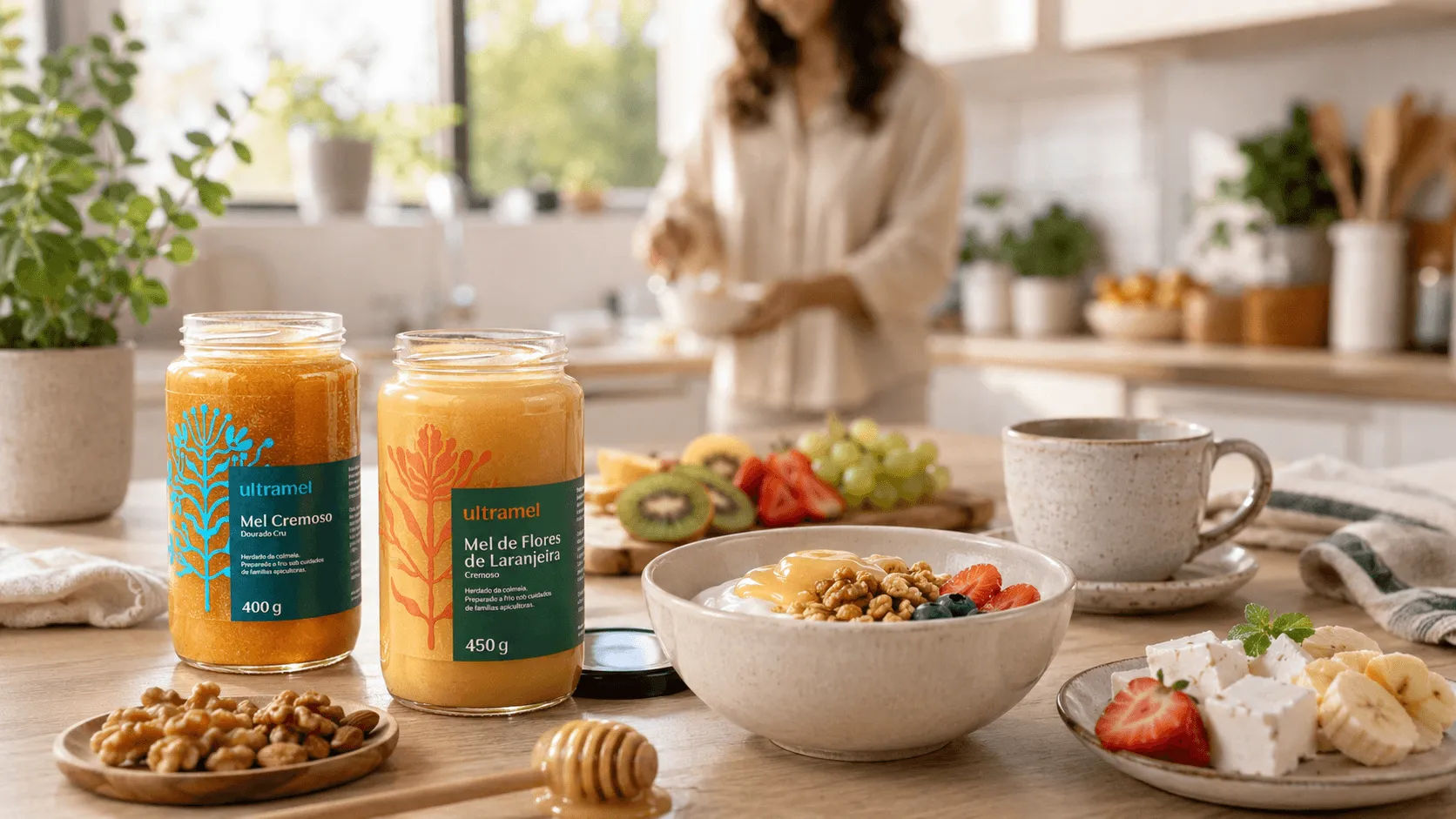 Dois potes de mel cremoso da marca Ultramel — Mel Cremoso Dourado Cru (400g) e Mel de Flores de Laranjeira Cremoso (450g) — sobre uma bancada de cozinha clara, ao lado de uma tigela de iogurte com granola e frutas frescas, nozes e uma xícara de café, compondo um café da manhã saudável.