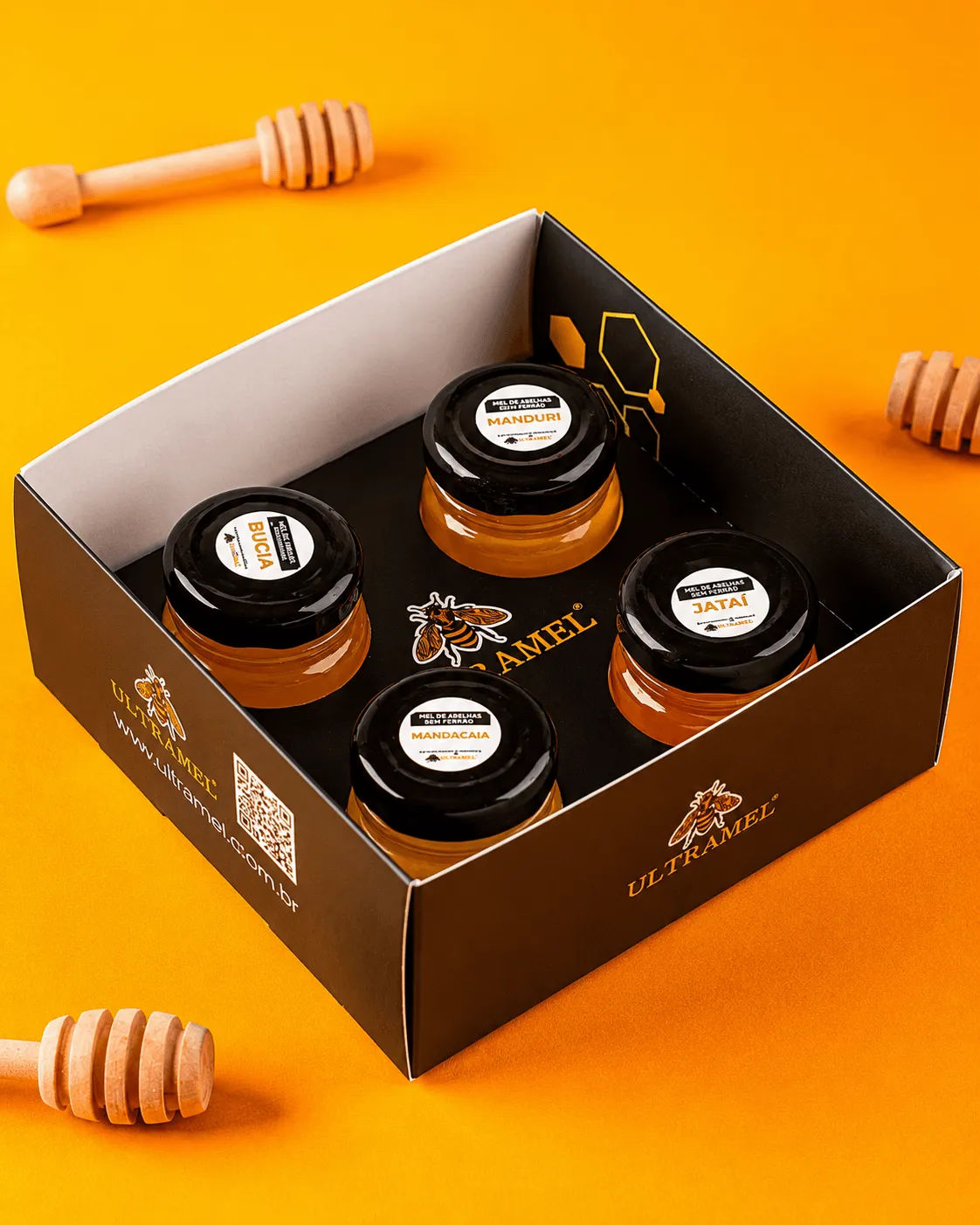 Kit de degustação Ultramel com quatro potes de mel de abelhas sem ferrão — Bucia, Manduri, Mandacaia e Jataí — dispostos em caixa preta sobre fundo laranja, acompanhados de colheres de madeira para mel.
