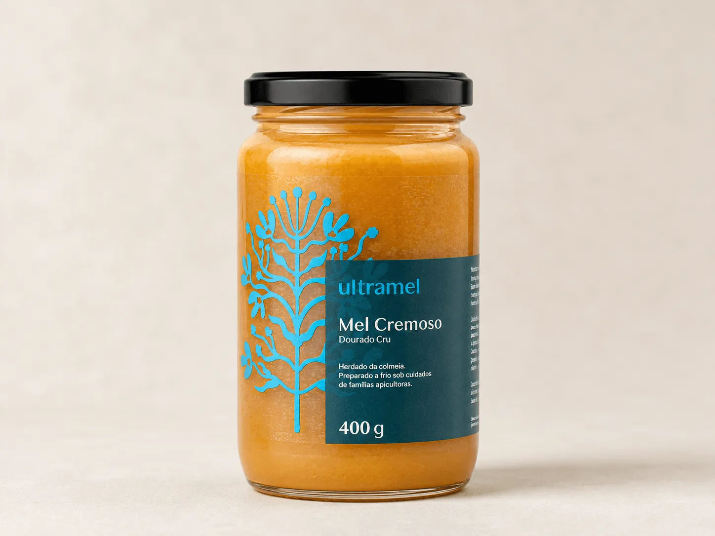 Pote de vidro de mel cremoso dourado cru da marca Ultramel, com 400g, rotulado em português com design botânico em azul turquesa. O produto é descrito como preparado a frio sob cuidados de famílias apicultoras.